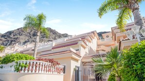 A residential building with a gated entrance, a balcony, and a mountain backdrop.
