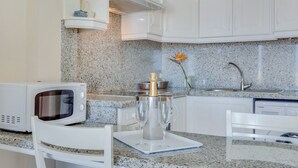 A kitchen with white cabinets, a granite countertop, a microwave, a coffee maker, and a vase with a flower.