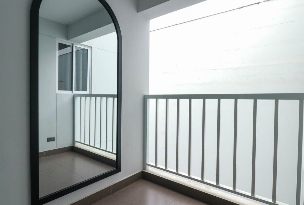 Une pièce dotée d’un grand miroir qui reflète une fenêtre et d’un balcon avec une rambarde en métal.