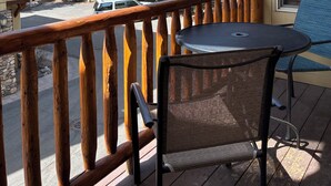 A wooden deck with a table and chair, overlooking a forested area and a mountain. - Lovin' Life. Near all the Fun Stuff! Now with A/C! (Ketchum)