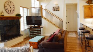 A living room with a fireplace, television, sofa, and a staircase leading to another level. - Lovin' Life. Near all the Fun Stuff! Now with A/C! (Ketchum)