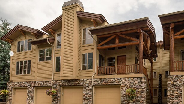 A multi-story house with a stone foundation, multiple garage doors, and a balcony with wooden railings. - Lovin' Life. Near all the Fun Stuff! Now with A/C! (Ketchum)