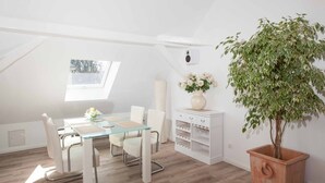 A modern loft bedroom with a glass dining table, white furniture, a large potted plant, and a skylight. - Holiday Apartment "Haus Behr am See" with 2 Balconies and Lake View (Radolfzell)