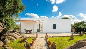 A white building with a stone pathway leading to a door, surrounded by rocks and greenery. - Cosy House in Cannigione with Terrace, Mountain Views (Arzachena)