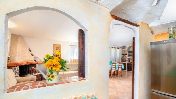 A kitchen with a refrigerator, a stone-tiled backsplash, and a window with a flower vase. - Cosy House in Cannigione with Terrace, Mountain Views (Arzachena)