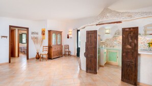 A spacious room with a tiled floor, wooden furniture, and a stone wall. - Cosy House in Cannigione with Terrace, Mountain Views (Arzachena)