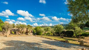 A paved courtyard with stone tiles, surrounded by greenery and trees. - Cosy House in Cannigione with Terrace, Mountain Views (Arzachena)