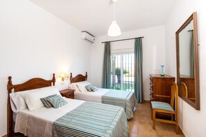 Habitació d'hotel amb dos llits, una cadira de fusta, un taulell, un mirall i una finestra amb cortines.