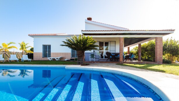 Une maison moderne dotée d’une piscine, d’un patio avec des chaises et d’un espace abrité.