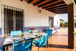 Terrassa exterior amb taula preparada per dinar, cadires blaves i zona de seients amb coixins.