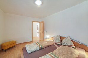A bedroom with a bed, a bench, a door, and a ceiling light. - Cosy Strickerhof Apartment 1 with Mountain View & Balcony (St. Leonhard in Passeier)