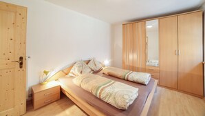 Een slaapkamer met een bed, een houten garderobe, nachtkastje en een nachttafel.