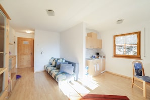 A room with a sofa, a chair, a kitchen area, and a wooden door. - Cosy Strickerhof Apartment 1 with Mountain View & Balcony (St. Leonhard in Passeier)