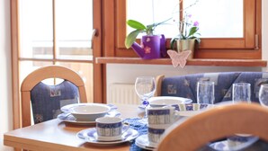 A dining table set with plates, cups, and a wine glass, with chairs and a window in the background. - Cosy Strickerhof Apartment 2 with Mountain View & Balcony (St. Leonhard in Passeier)