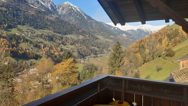 Une vue sur les montagnes depuis un balcon en bois, avec un ciel dégagé.