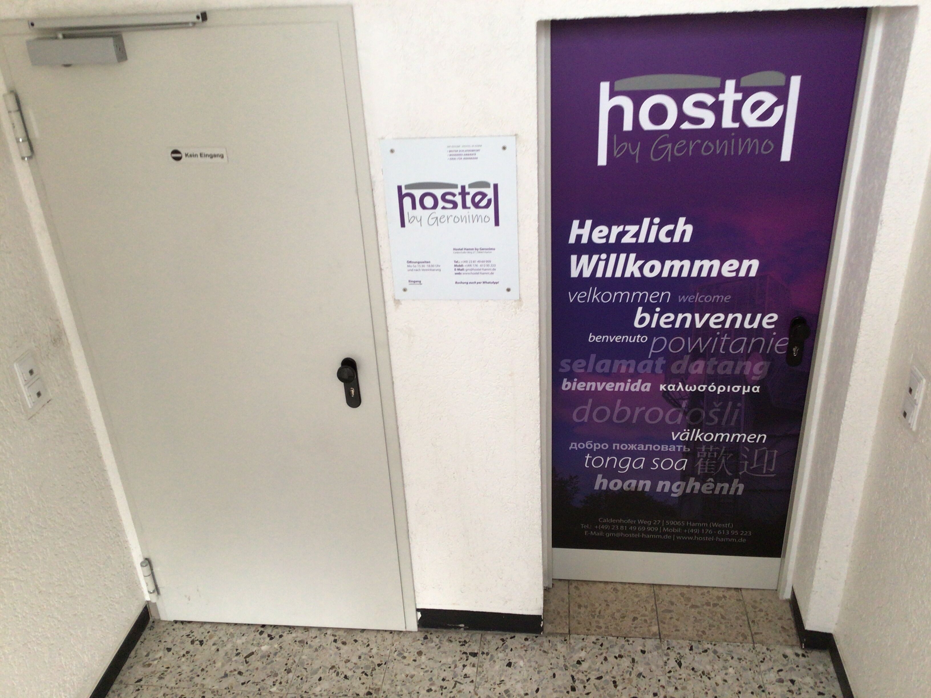 A hostel entrance with a signboard displaying multilingual welcome messages and contact information.