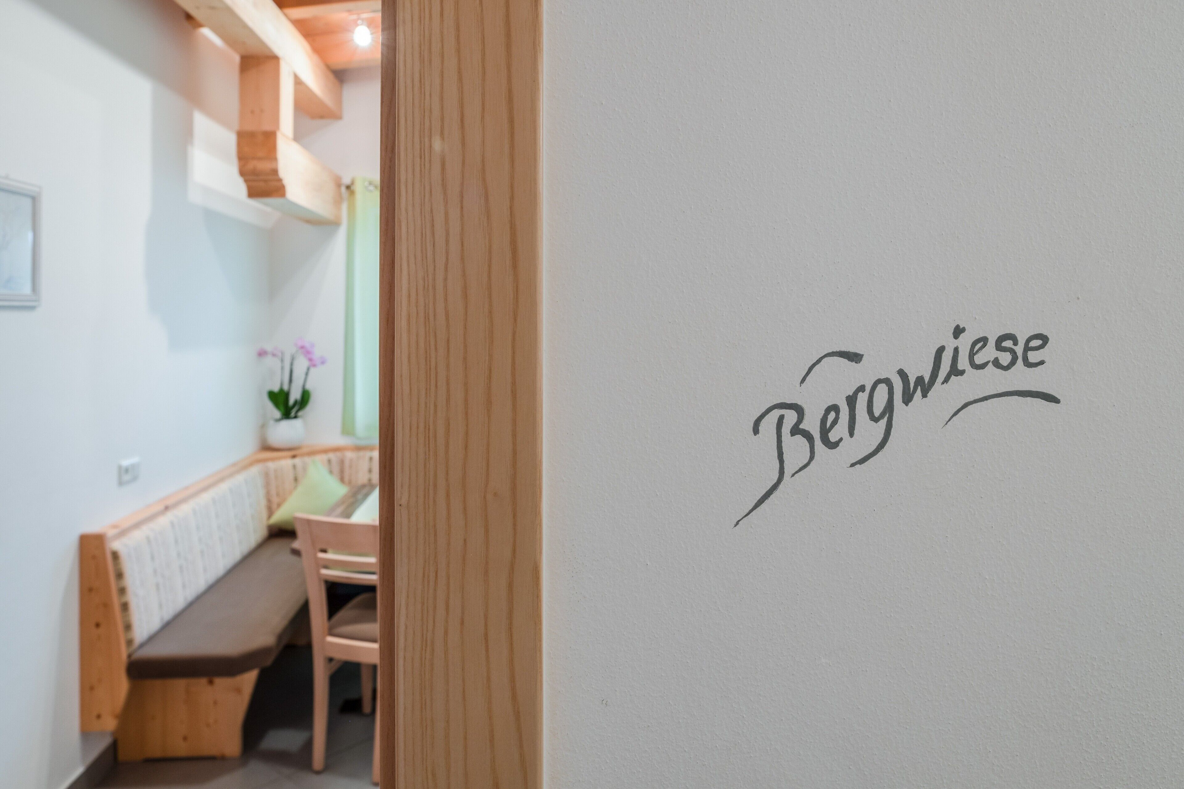Ein Zimmer mit einer Holzbank, einem kleinen Tisch und einer Wand mit dem Schriftzug 'Bergwiese'.