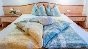 A neatly made bed with a heart-shaped pillow, a wooden headboard, and bedside tables with lamps. - Holiday Apartment 'Hofschenke Pfeiftal - Bergwiese' with Mountain View (St. Martin in Passeier)