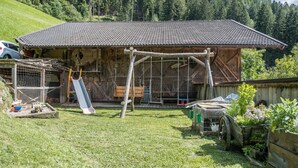 A rustic wooden building with a tiled roof, a swing set, and a fenced area with a cat. - Holiday Apartment 'Hofschenke Pfeiftal - Bergwiese' with Mountain View (St. Martin in Passeier)