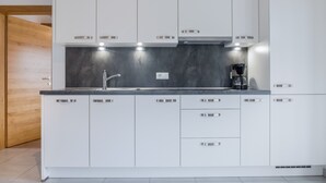 A modern kitchen with white cabinets, a black countertop, and a coffee maker. - Ferienwohnung "Hofschenke Pfeiftal Bergblick" mit Terrasse, Garten & WLAN (St. Martin in Passeier)