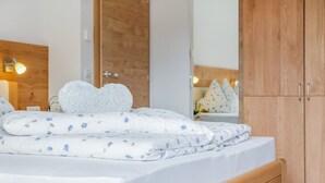 A neatly made bed with a heart-shaped pillow, a wooden headboard, and a wardrobe with a mirror. - Ferienwohnung "Hofschenke Pfeiftal Bergblick" mit Terrasse, Garten & WLAN (St. Martin in Passeier)