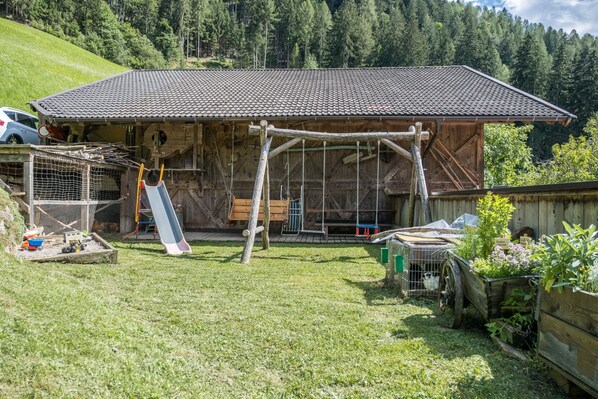 A rustic wooden building with a tiled roof, a swing set, and a fenced area with a cat.