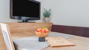 A modern living room with a flat-screen TV, a wooden bowl of fruit, a notebook, and a small plant. - Ferienwohnung "Hofschenke Pfeiftal Bergblick" mit Terrasse, Garten & WLAN (St. Martin in Passeier)