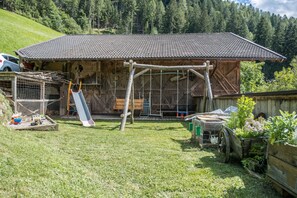 Ein rustikales Holzhaus mit Ziegeldach, einer Schaukel und einem eingezäunten Bereich mit einer Katze.