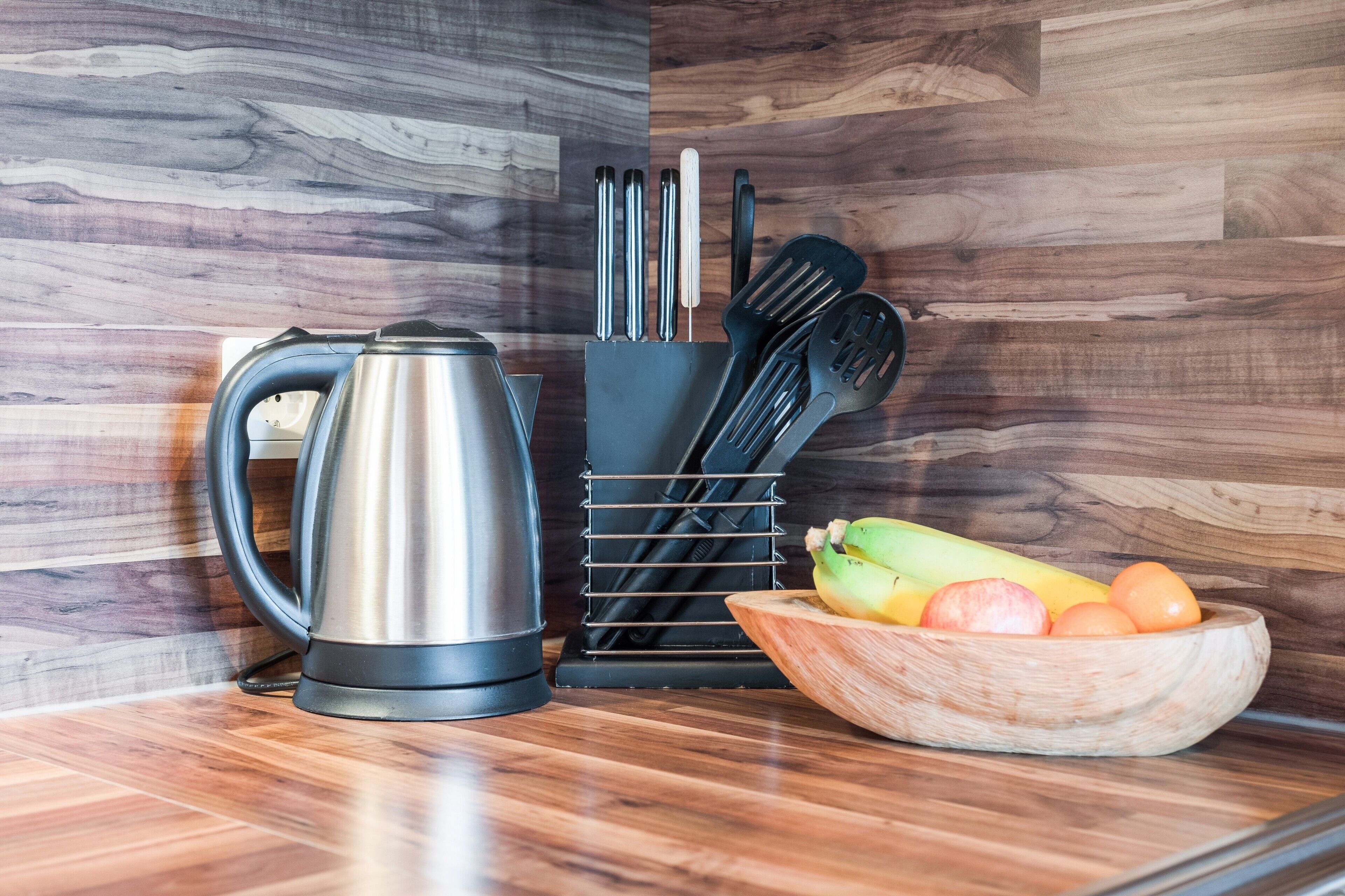 A kitchen counter with a kettle, a knife block, and a bowl of fruit.
