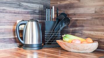 A kitchen counter with a kettle, a knife block, and a bowl of fruit.