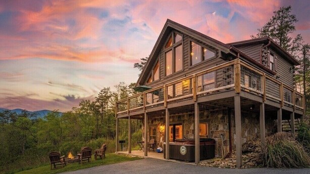 A large log cabin with a second-story balcony, a fireplace, and a stone fireplace surround.