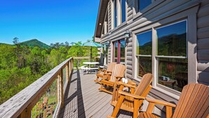 A wooden deck with Adirondack chairs and a table, overlooking a forested landscape.