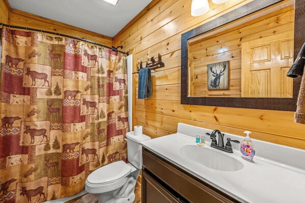 A bathroom with a wooden interior, a shower curtain with animal prints, a toilet, a sink with a mirror, and a towel rack.