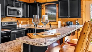 A kitchen with wooden cabinets, a granite countertop, and two wine glasses on a cutting board.