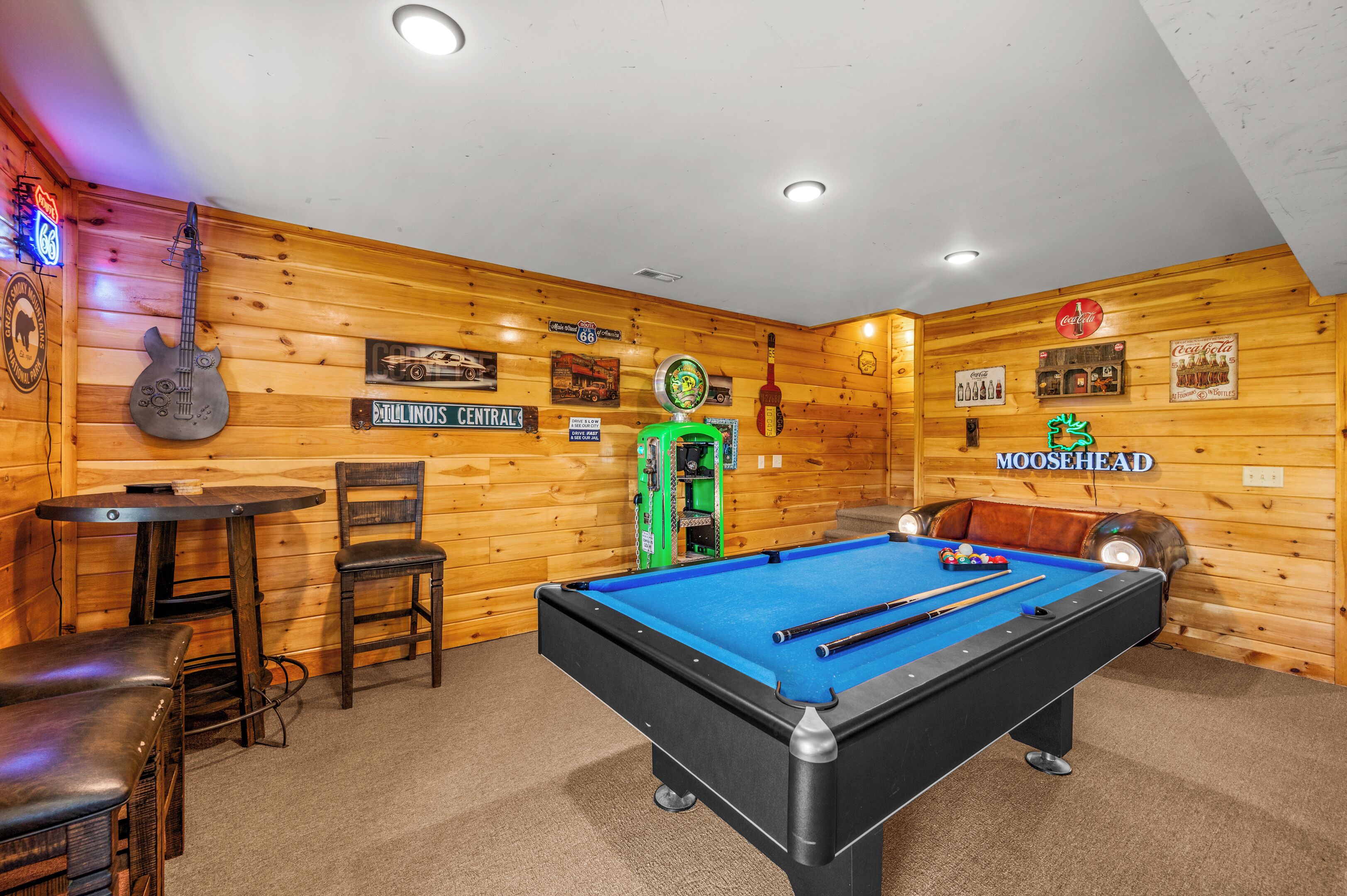 A pool table in a room with wooden walls, a pool cue, and a billiard ball rack.