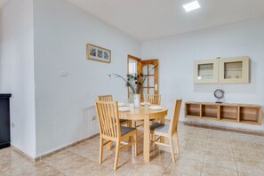 Un comedor con una mesa redonda, sillas de madera, un jarrón con plantas secas y un mueble con puertas de vidrio.
