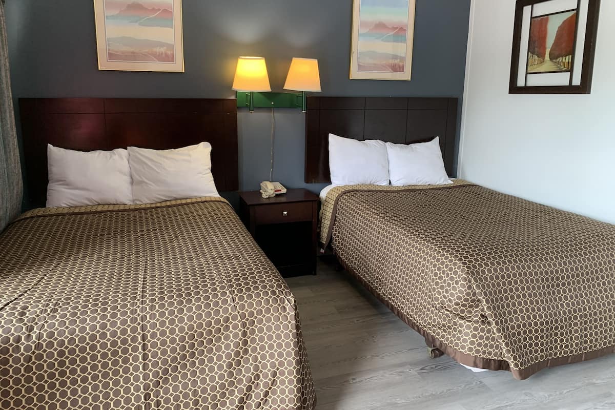 Ein Hotelzimmer mit zwei Betten, einem Nachttisch, einer Lampe und gerahmten Bildern an den Wänden.