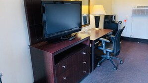 Habitación de hotel con televisor de pantalla plana sobre un soporte de madera, un escritorio con una silla, una lámpara y un microondas.