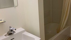 Un baño con lavamanos blanco, un espejo y zona de ducha.