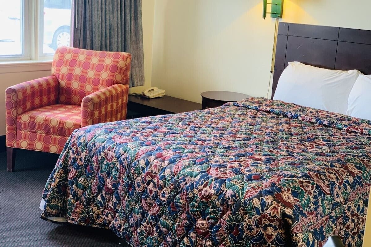 Ein Hotelzimmer mit einem großen Bett, einem Sessel, einer Lampe und einem Fenster mit Vorhängen.