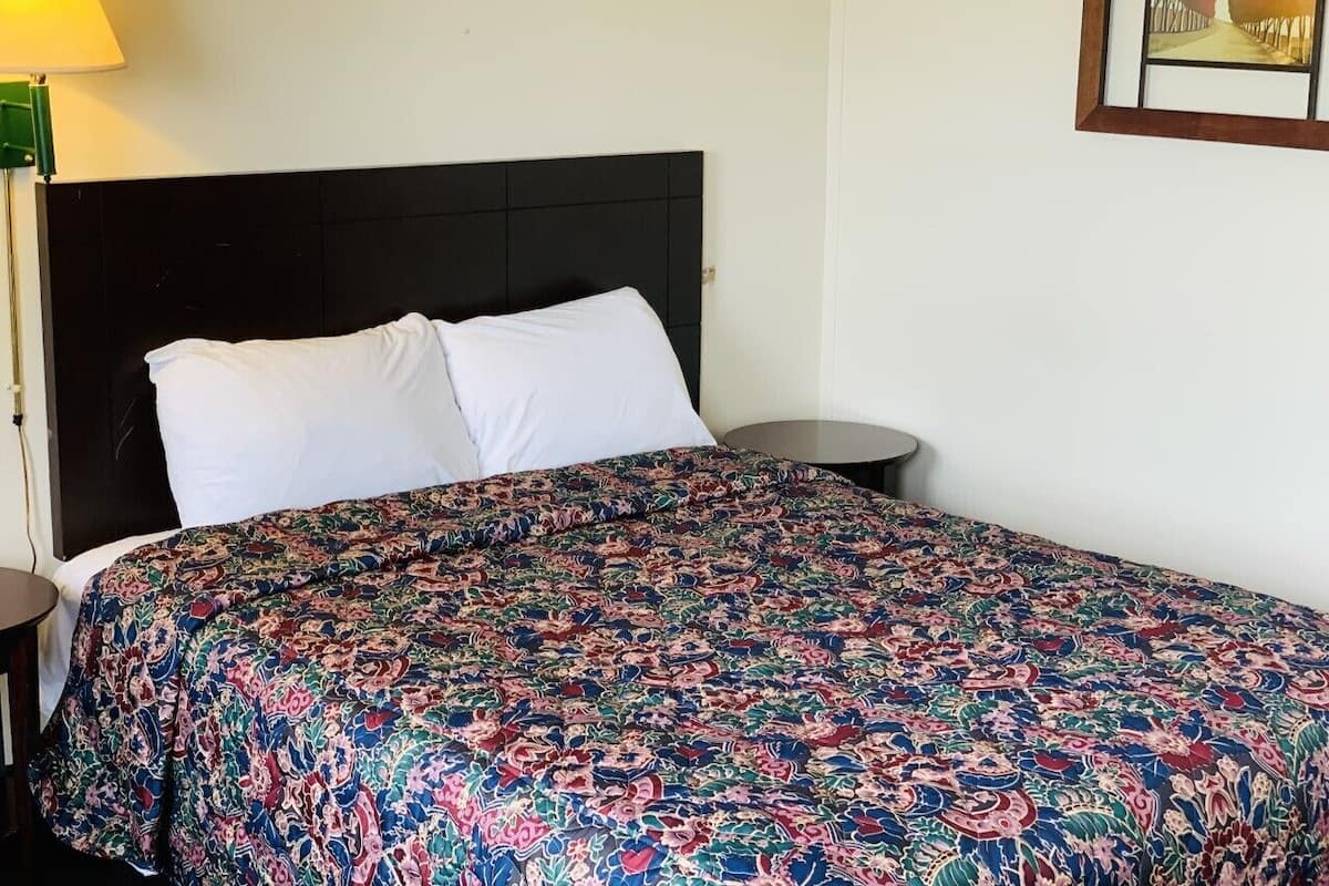 Ein Bett mit einem gemusterten Überwurf, ein Nachttisch und eine Lampe.