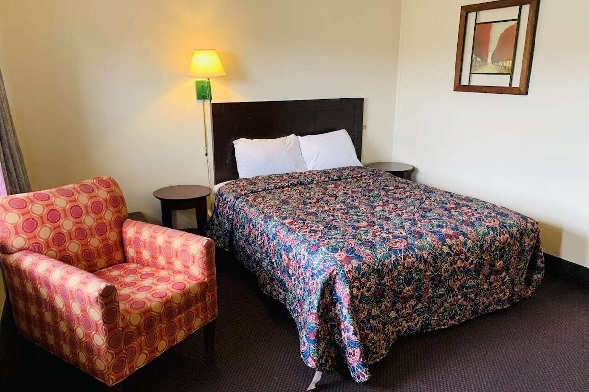Ein Hotelzimmer mit Bett, Stuhl, Nachttisch und Lampe.