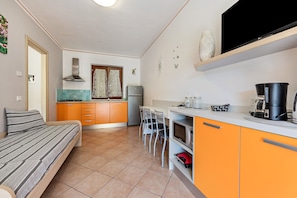 Une petite cuisine équipée, avec un lit, un coin repas et un téléviseur fixé au mur.