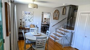 Un coin repas avec une table ronde et des chaises, un escalier et une porte dotée de volets à persiennes.