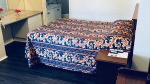Quarto com cama, escrivaninha, cadeira, televisão e quadro na parede.