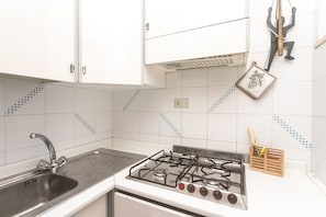 A kitchen with white cabinets, a stainless steel sink, a gas stove, and a tiled backsplash with blue patterns.