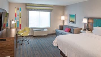 Ein Hotelzimmer mit Bett, Schreibtisch, Stuhl, Sofa, Fenster und einer Wand mit vertikalen Streifen.