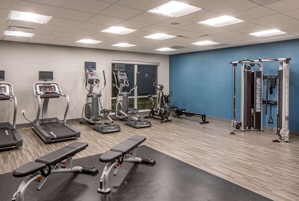 Un gimnasio con cintas de correr, elípticas y equipo de levantamiento de pesas.