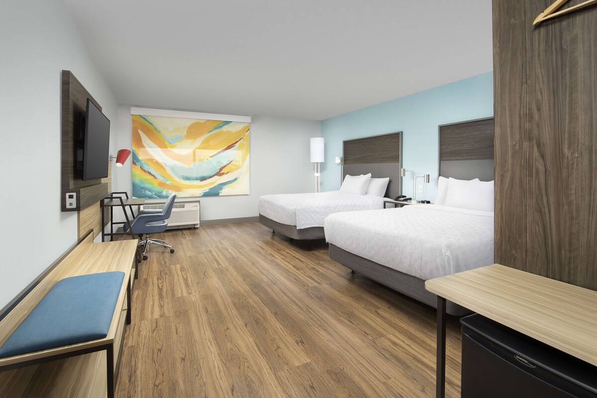 Hotelkamer met twee bedden, een bureau, een stoel, een televisie en een groot abstract schilderij aan de muur.