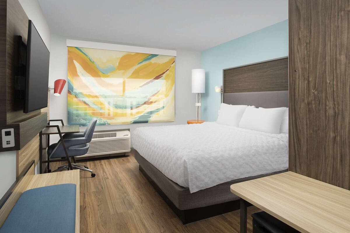 Een moderne hotelkamer met een groot bed, een bureau, een stoel, een flatscreen-tv, een groot abstract schilderij, een lamp en een raam met uitzicht.